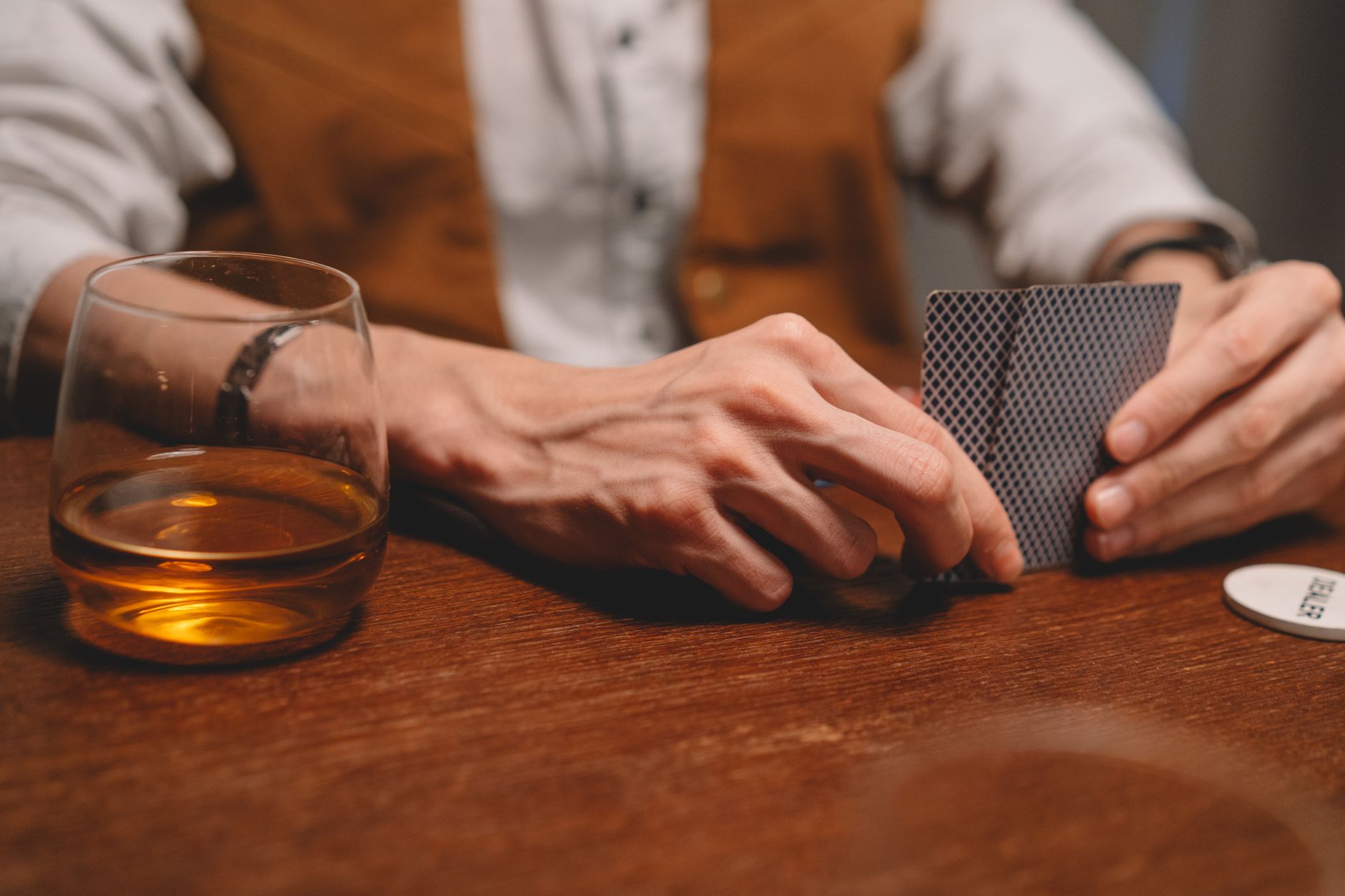Gros plan de mains tenant des cartes à jouer avec du whisky sur la table, parfait pour les thèmes du jeu et des loisirs.